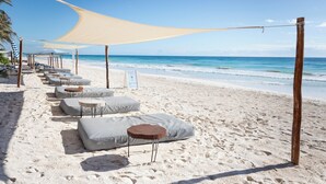 A beachside seating area with lounge chairs and tables under a canopy, overlooking the ocean. - Lula Tulum, a Small Luxury Hotel (Tulum)