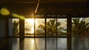 Une pièce spacieuse avec une grande fenêtre donnant sur des palmiers et un coucher de soleil.