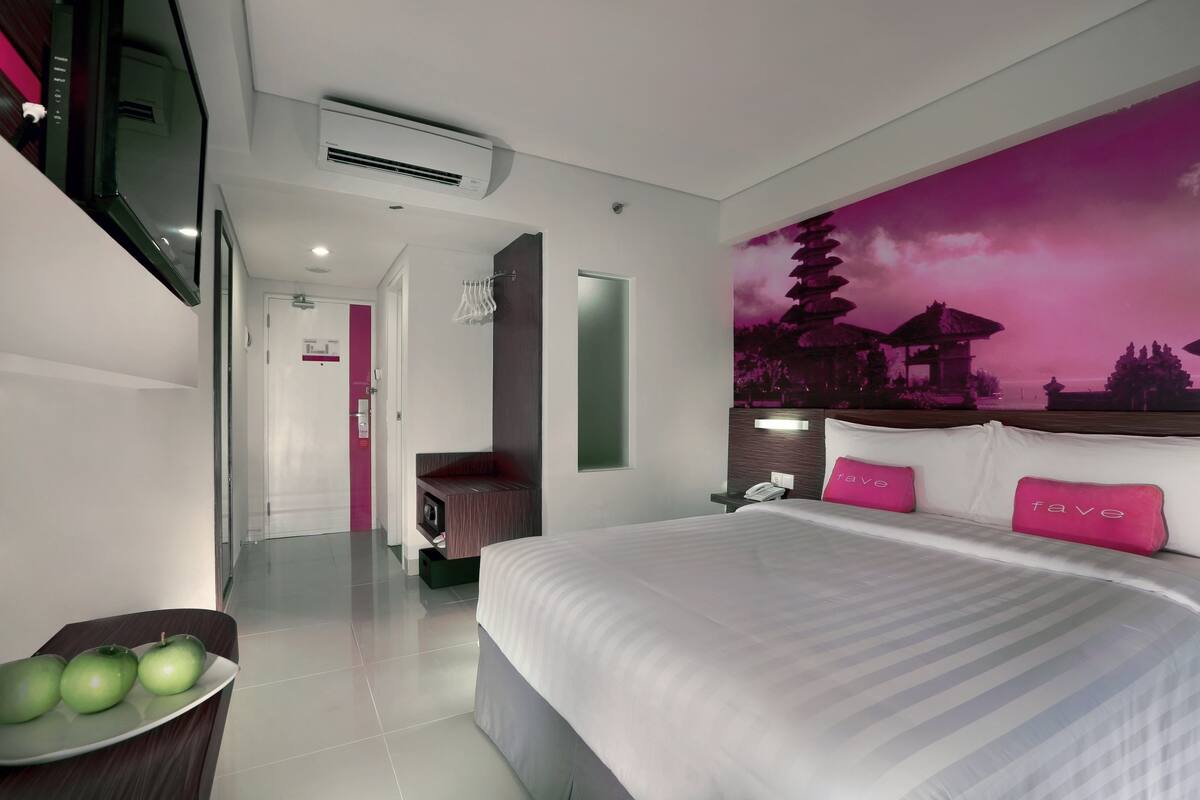 A modern hotel room with a bed, a TV, a wall-mounted air conditioner, and a decorative wall mural.