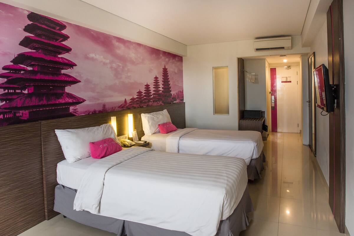 A hotel room with two beds, a large wall mural of a pagoda, a TV mounted on the wall, and a hallway leading to the bathroom.