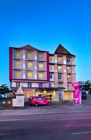 Um hotel de vários andares com uma placa grande 'favehotel', uma área de estacionamento com um carro rosa e uma estátua em frente.