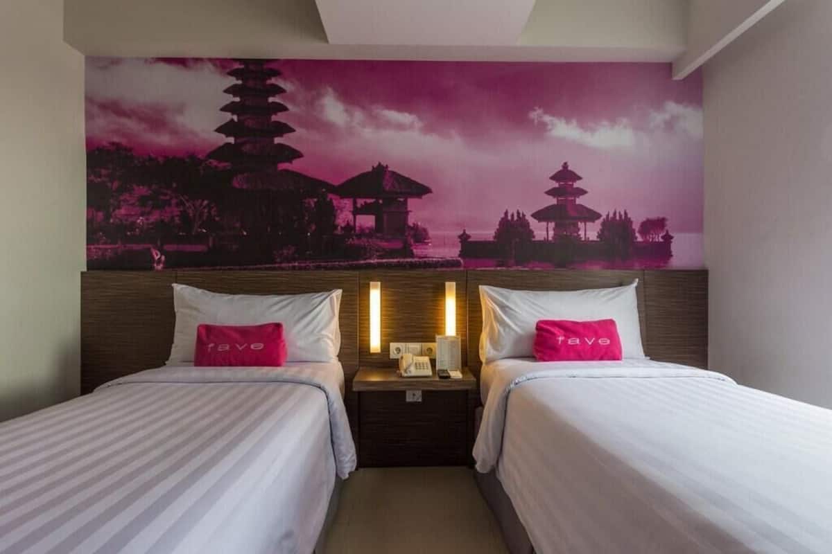 A hotel room with two beds, a nightstand with a lamp, and a wall mural of pagodas.