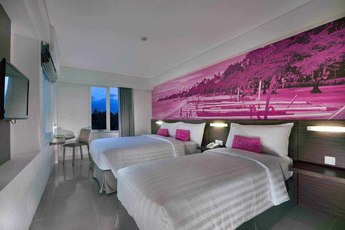 A hotel room with two beds, a desk, a chair, a TV, and a large pink mural on the wall.