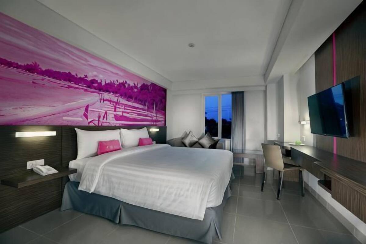 A modern hotel room with a large bed, a desk, a television, and a view of the sky.