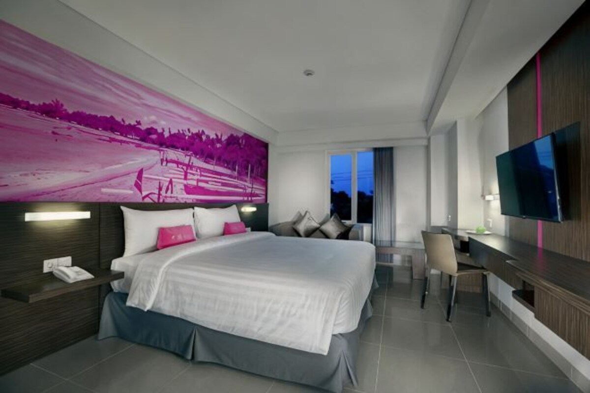 A modern hotel room with a large bed, a desk, a television, and a view of the sky.