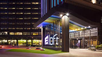 Una entrada de hotel moderna con un llamativo letrero que dice 'a loft', fachada de vidrio y un área de recepción bien iluminada.