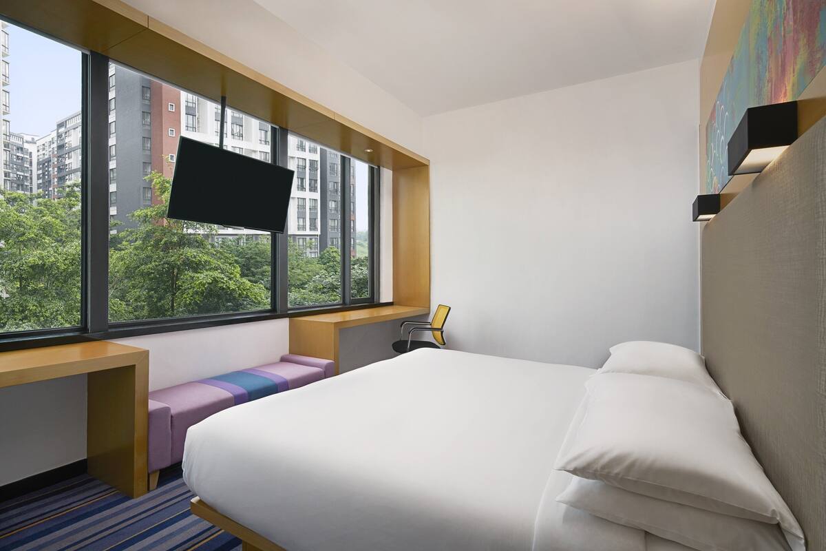 Une chambre d’hôtel avec une grande fenêtre, un lit, un bureau et une chaise.