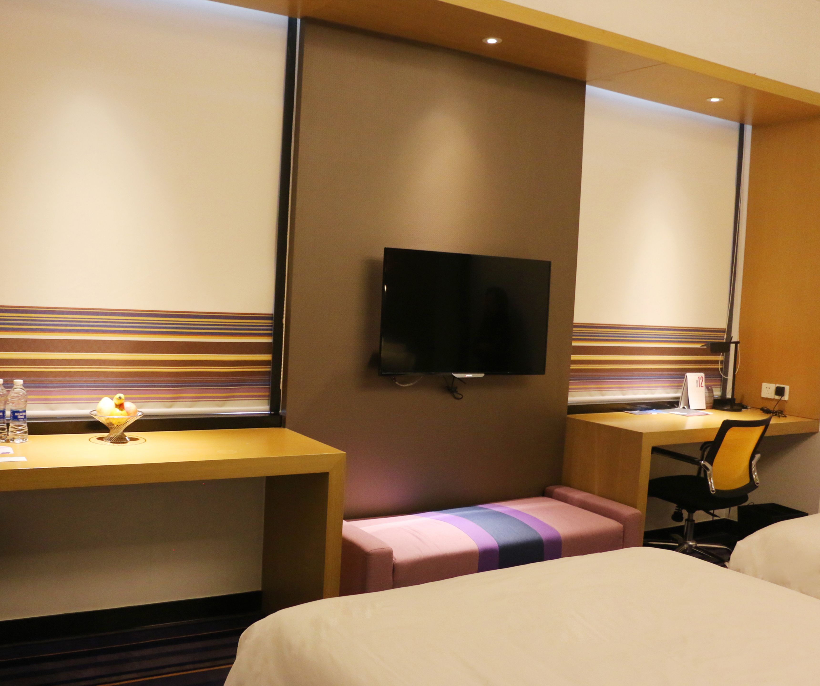 A hotel room with a bed, a desk, a television, and a bench.