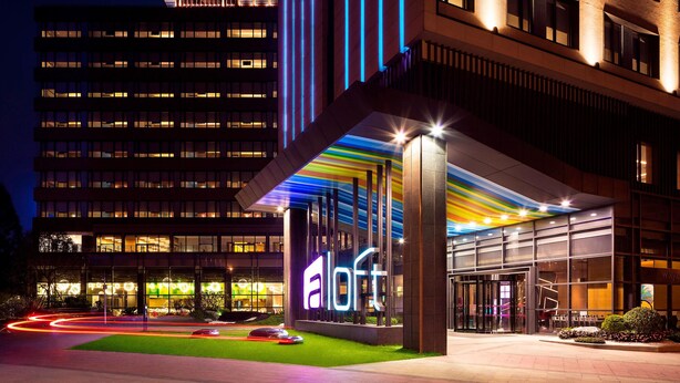 A modern hotel entrance with a prominent 'a loft' sign, large windows, and a well-lit facade. - Aloft Guangzhou University Park (Guangzhou)