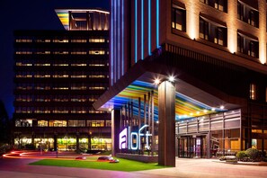 A modern hotel entrance with a prominent 'a loft' sign, large windows, and a well-lit facade.
