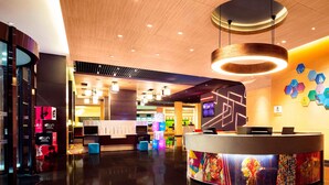 A modern hotel lobby with a reception desk, a wooden ceiling, and a colorful wall mural. - Aloft Guangzhou University Park (Guangzhou)