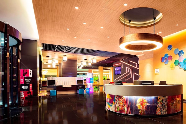 A modern hotel lobby with a reception desk, a wooden ceiling, and a colorful wall mural.