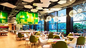 A modern restaurant with high ceilings, geometric ceiling lights, and large windows offering views of greenery. - Aloft Guangzhou University Park (Guangzhou)