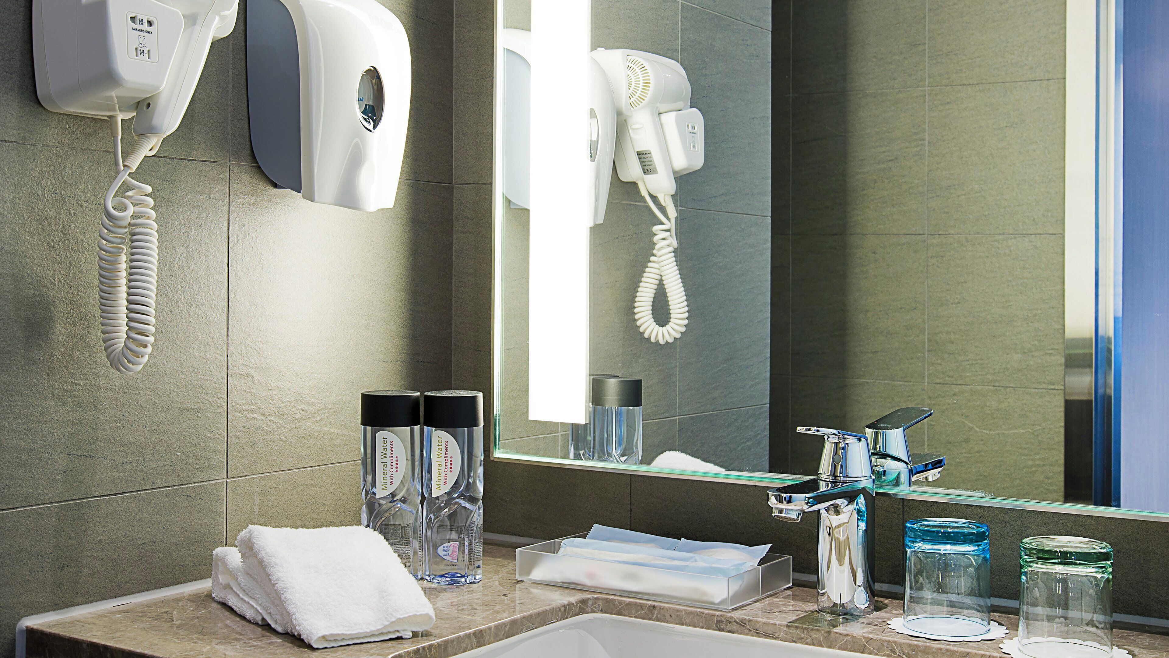 A hotel bathroom with a sink, mirror, towel, and amenities like a hair dryer and phone.