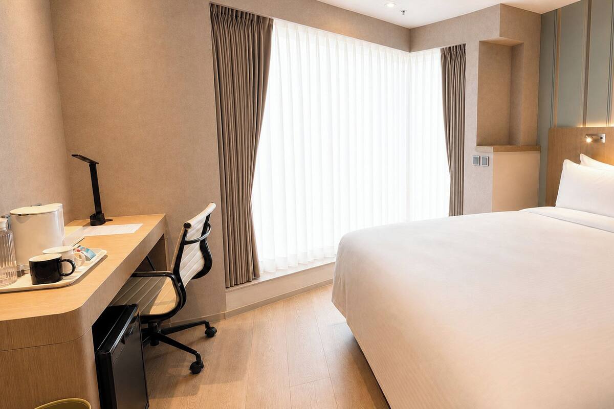 A hotel room with a bed, desk, chair, and curtains.