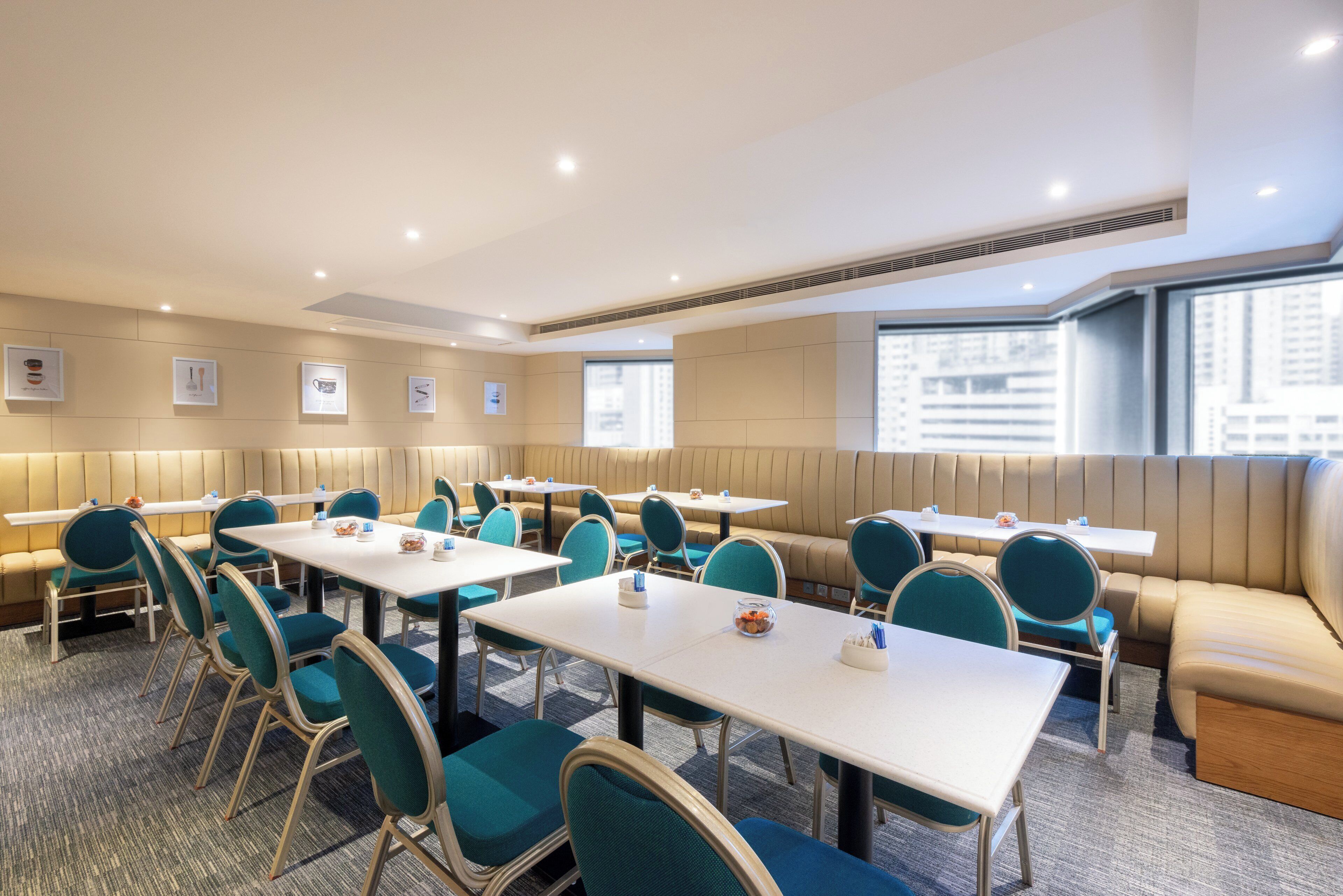 Un salón de conferencias con varias mesas y sillas, un techo alto con iluminación empotrada y vistas a la ciudad a través de amplios ventanales.