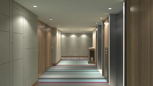 Un pasillo de hotel con paneles de madera, alfombra a rayas y un pequeño escritorio de madera con una silla.