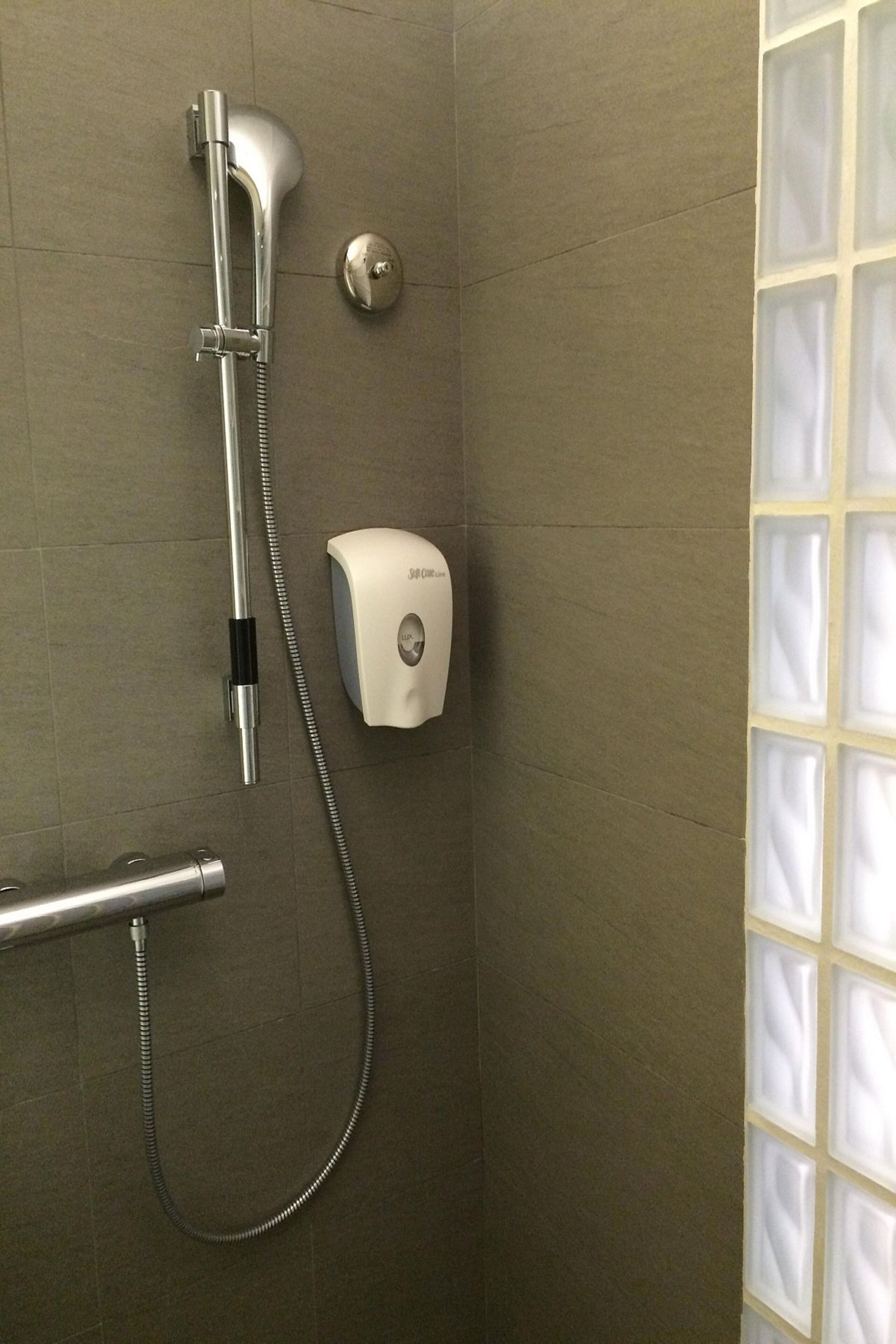 A shower with a handheld showerhead, a handheld shower attachment, and a soap dispenser on the wall.