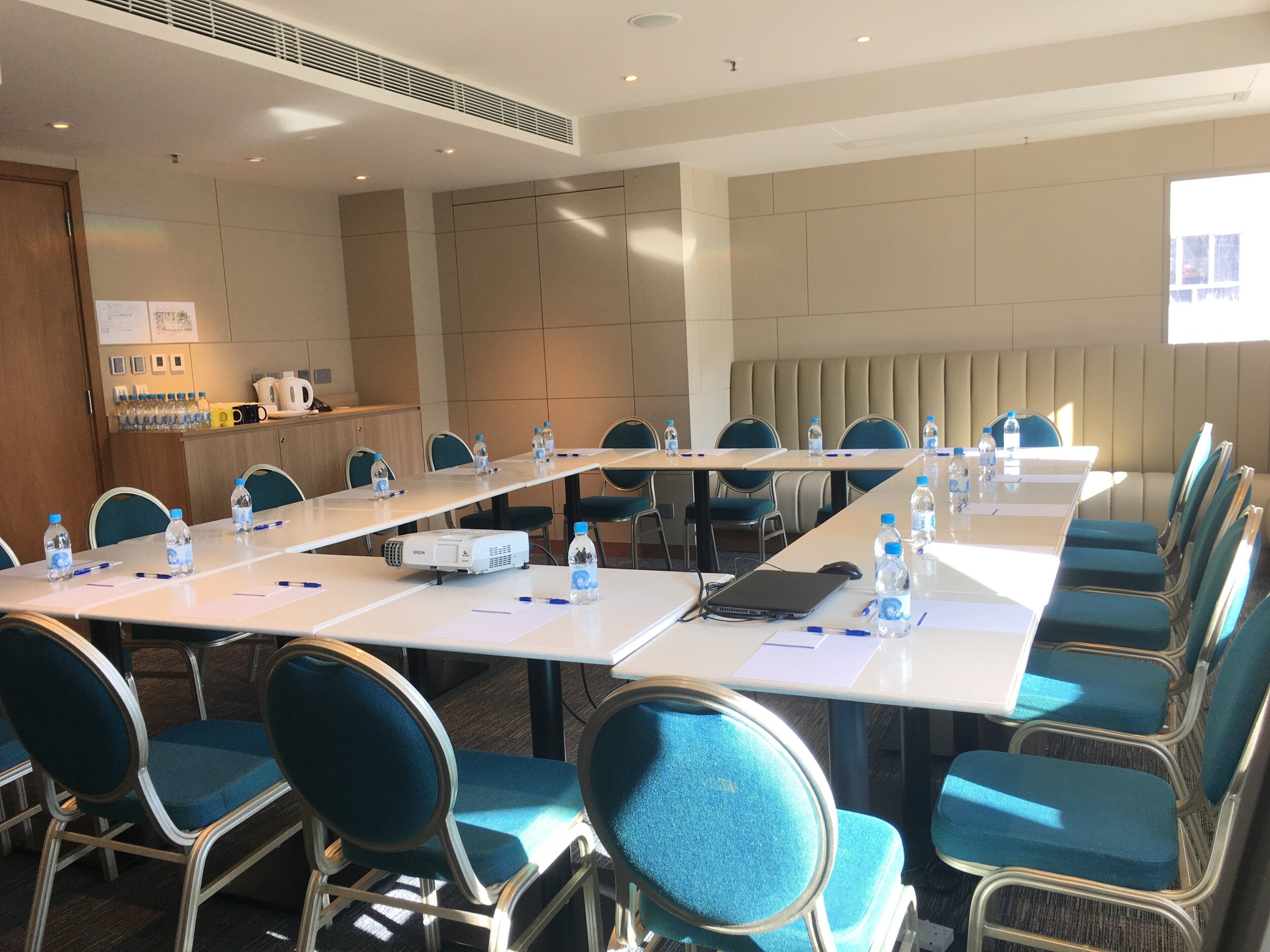 Un salón de conferencias con una larga mesa, sillas, botellas de agua, un proyector y una computadora portátil.