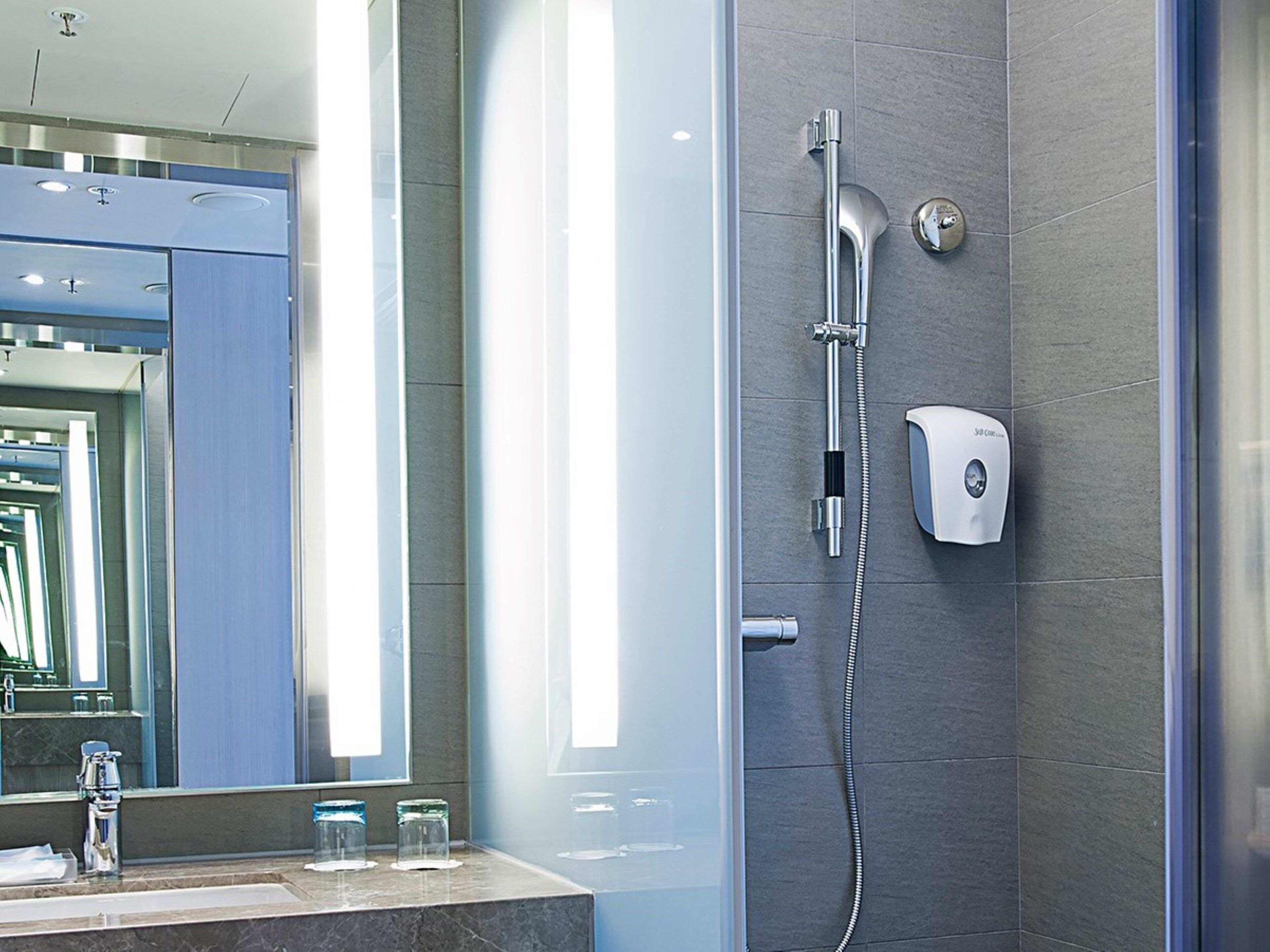 A modern bathroom with a glass shower enclosure, a handheld showerhead, a wall-mounted faucet, and a soap dispenser.