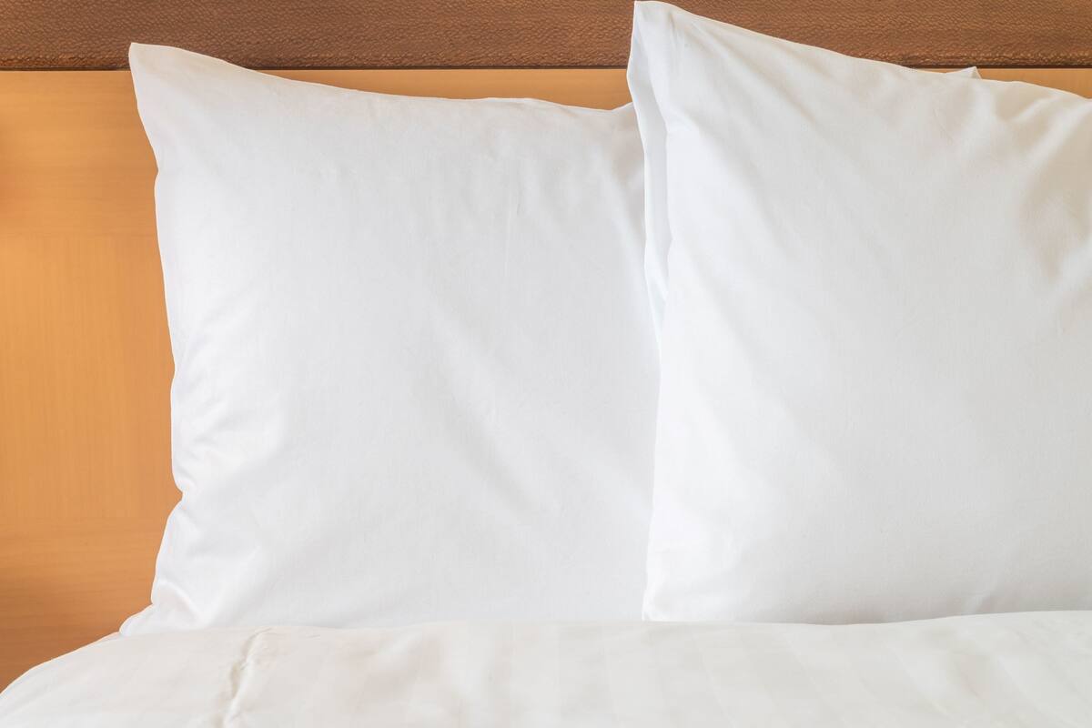 A bed with white bedding and pillows against a wooden headboard.