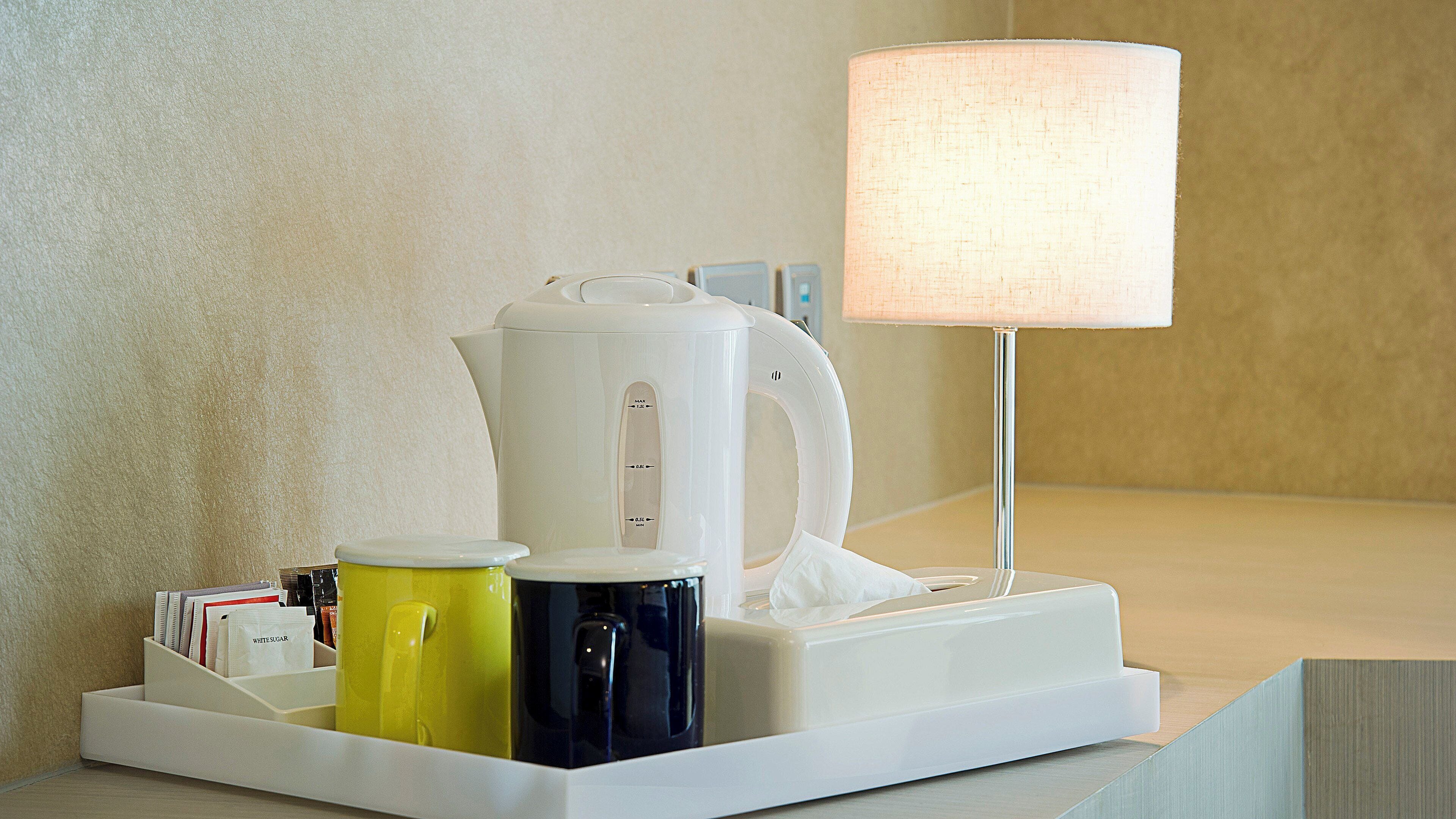 A coffee maker, a lamp, and a tray with cups and a tissue box on a table.