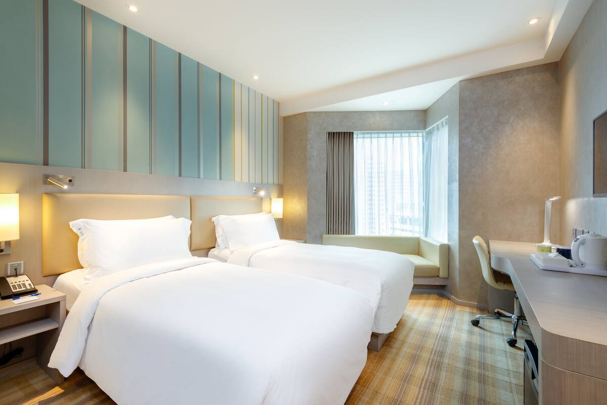 A hotel room with two beds, a desk, a chair, and a window with curtains.
