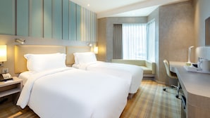 Habitación de hotel con dos camas, un escritorio, una silla y una ventana con cortinas.