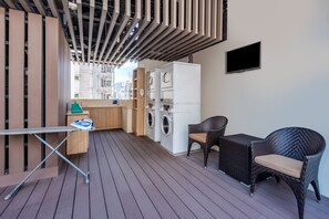A compact laundry area with a washing machine and dryer, a small table with a shoe rack, and two wicker chairs.