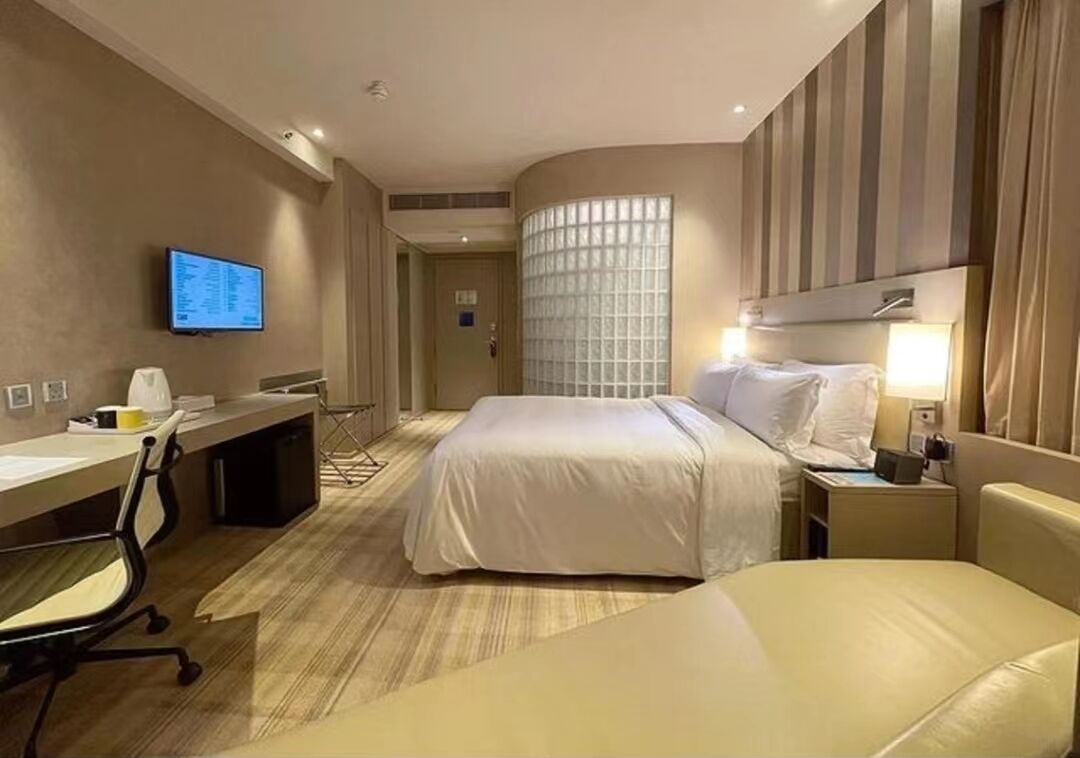 Habitación de hotel con cama, escritorio, silla, televisor y ventana con persianas.