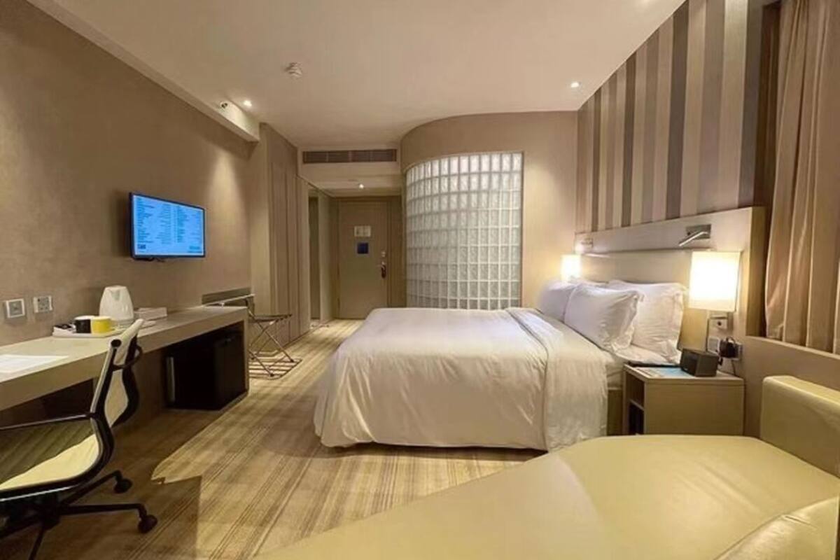 A hotel room with a bed, a desk, a chair, a TV, and a window with blinds.