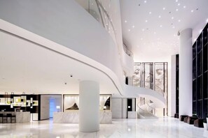 A modern hotel lobby with a curved ceiling, a central marble column, and a staircase leading to upper floors. - Ziyuan Hotel (Wuhan)
