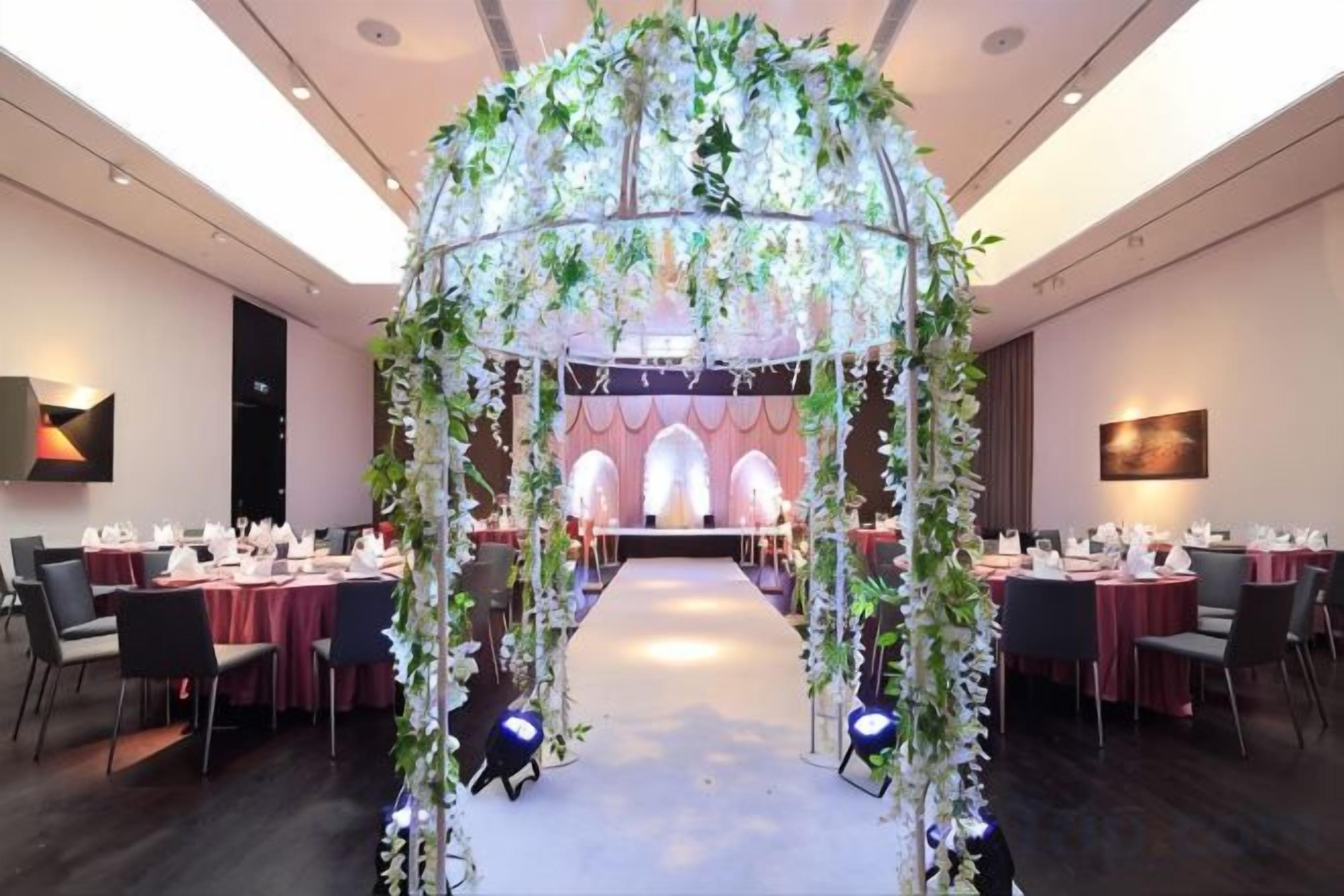 Un salón de banquetes con un pasillo central, mesas a ambos lados y un arco decorativo.