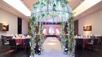 Un salón de banquetes con un pasillo central, mesas a ambos lados y un arco decorativo.