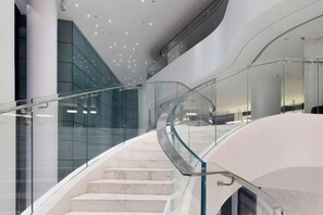 A modern interior with a curved glass railing, marble steps, and a high ceiling with recessed lighting. - Ziyuan Hotel (Wuhan)