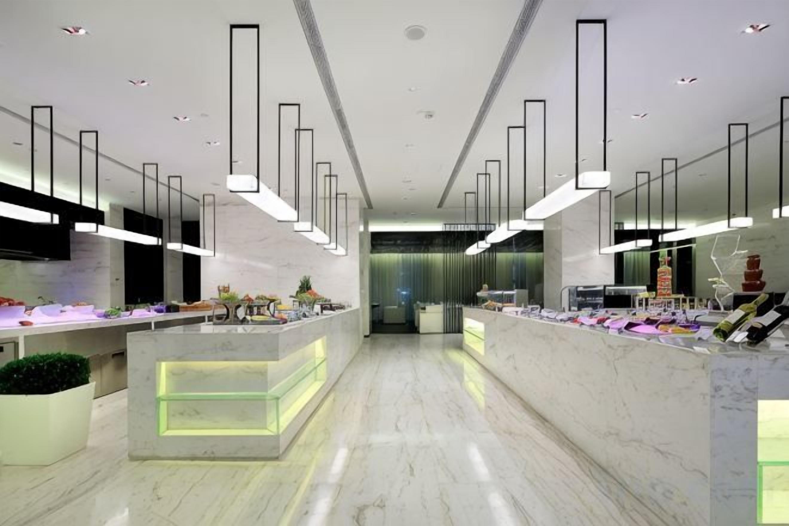 Un moderno vestíbulo de hotel con piso de mármol, una recepción y lámparas colgantes.