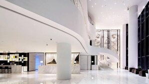 Una moderna hall d'albergo con soffitto a volta, pavimento in marmo e reception con schermo digitale.