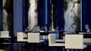 Un restaurant où les tables sont dressées pour le service, avec des colonnes en marbre et une grande fresque murale.