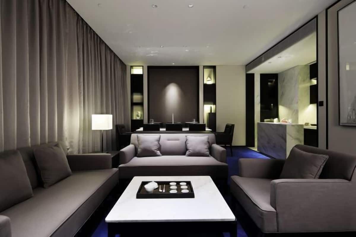 A modern hotel room with a sofa set, a coffee table, and a seating area with a TV.