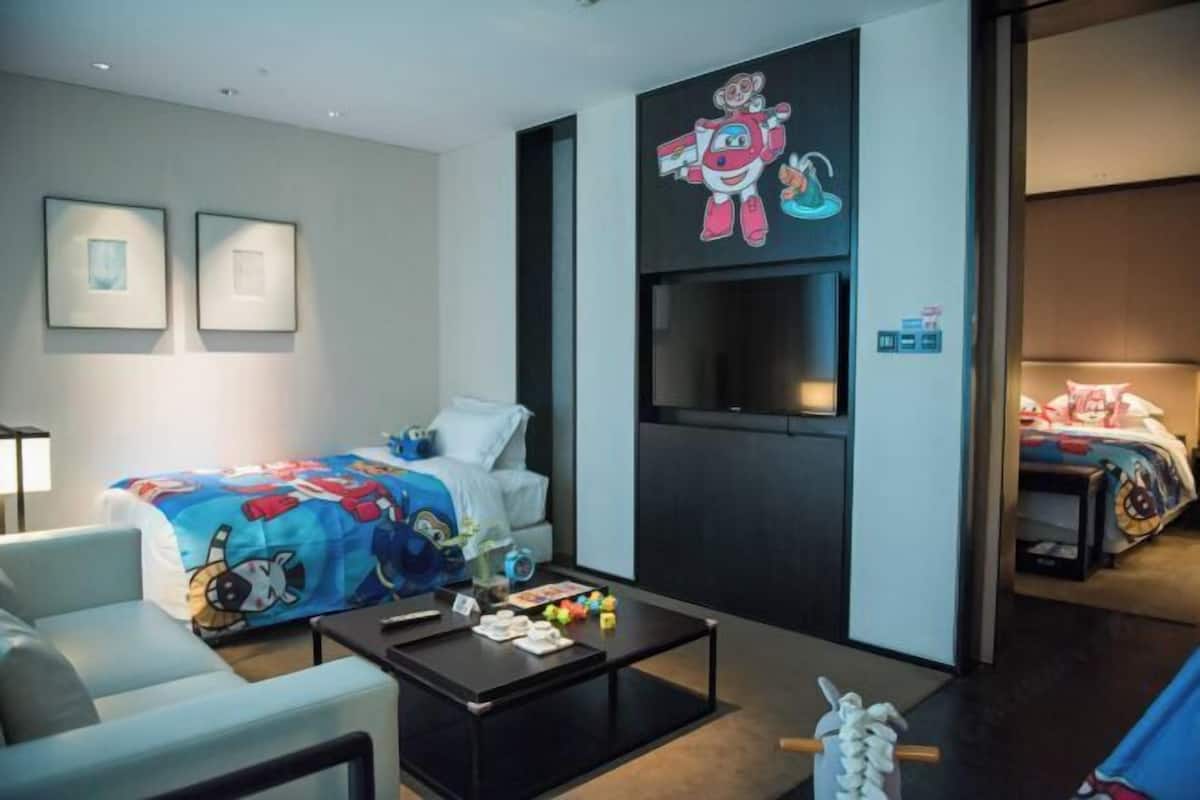 A hotel room with a bed, a sofa, a coffee table, a TV, and a wall with cartoon characters.