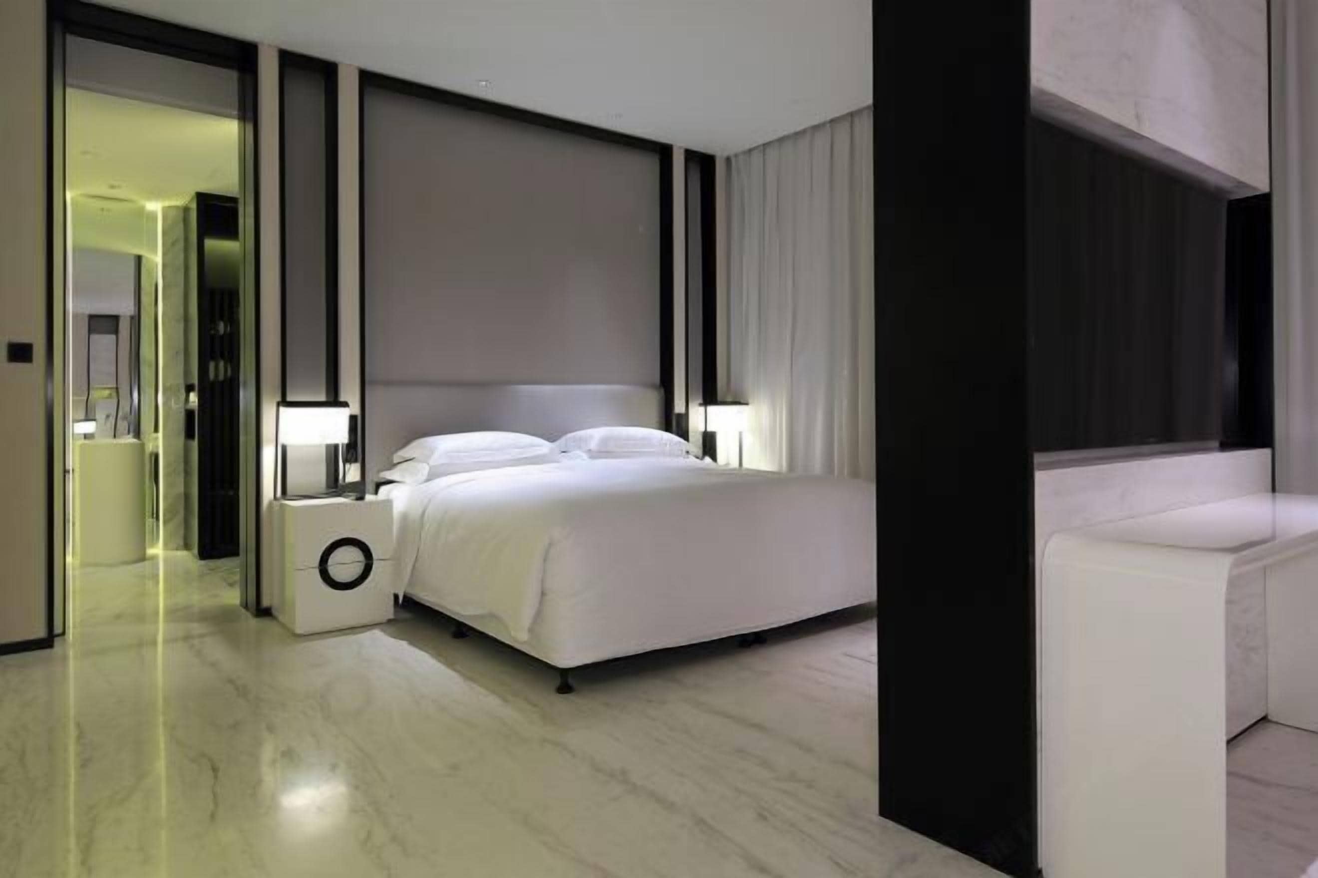 Una habitación de hotel moderna con una cama grande, lámparas de noche, una mesita auxiliar pequeña y un vestidor.