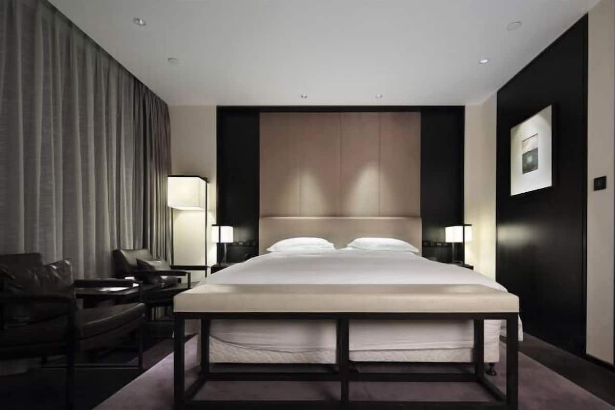 A modern hotel room with a large bed, a desk, a chair, and a lamp.
