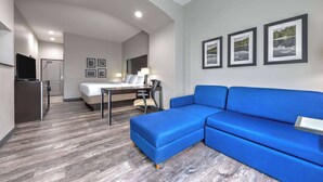 A modern hotel room with a blue sofa, a bed, a desk with a chair, and a TV. - La Quinta Inn & Suites by Wyndham Tyler - University Area (Tyler)