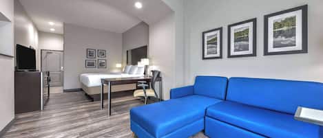 A modern hotel room with a blue sofa, a bed, a desk with a chair, and a TV.