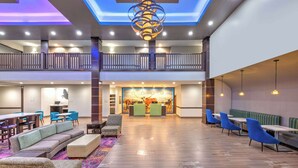 A spacious lobby with a high ceiling, a central reception desk, and seating areas. - La Quinta Inn & Suites by Wyndham Tyler - University Area (Tyler)