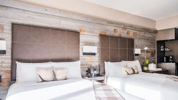 A hotel room with two beds, a wooden accent wall, a small bedside table with a lamp, and a coffee machine.