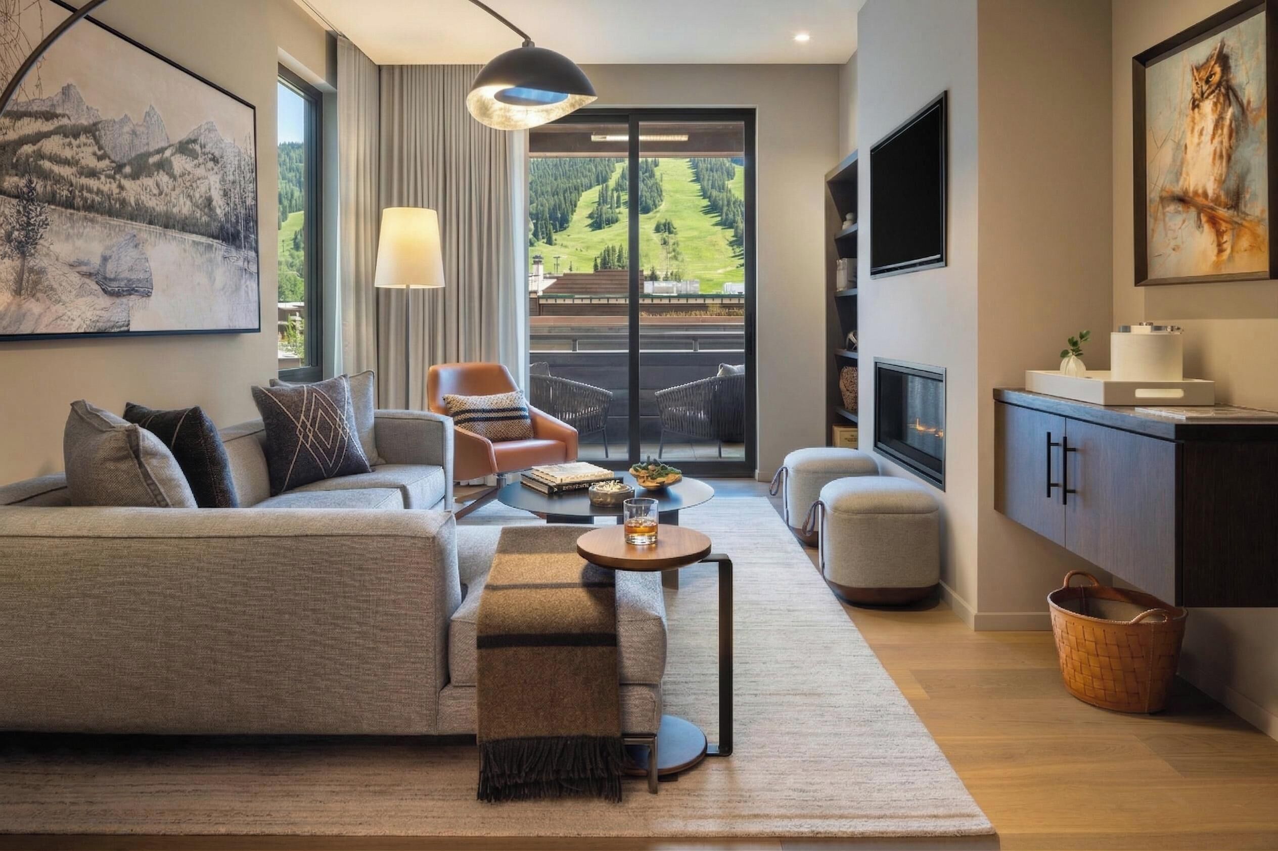 A modern living room with a sofa, armchair, and coffee table, a fireplace, and a large window with a mountain view.