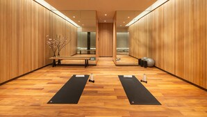 A modern, well-lit room with wooden walls, a central bench, two yoga mats, and exercise balls.