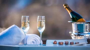 Two glasses of white wine, a bottle of champagne, and a tray with nuts on a table with a towel and a silver container.