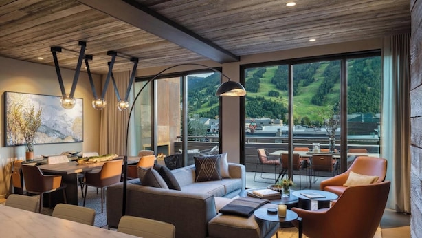 A modern hotel lobby with a wooden ceiling, large windows with a view of a green landscape, a dining area with a table and chairs, and a seating area with sofas and armchairs. - Hotel Jackson (Jackson)